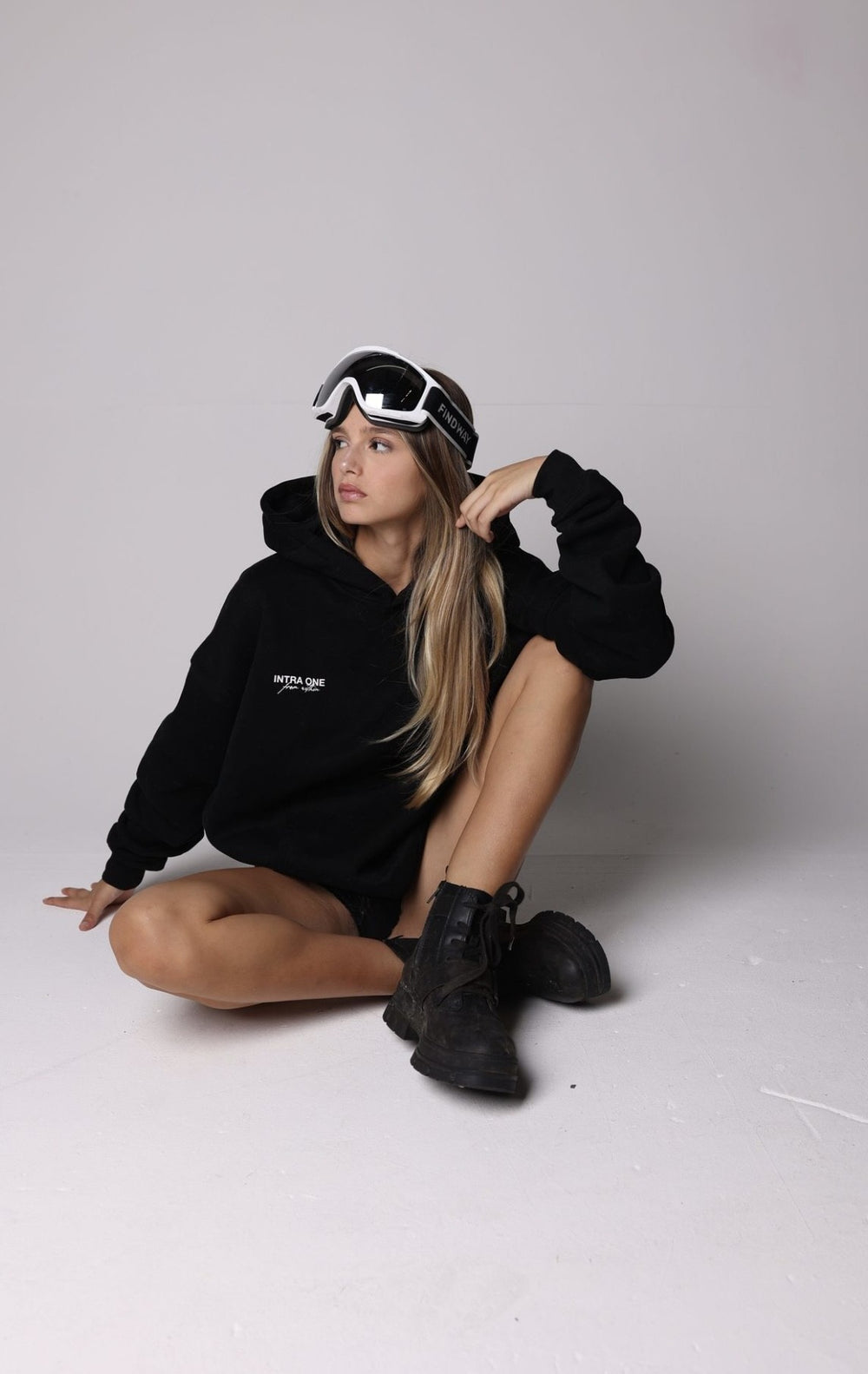 _christina_bliss_  sitting, wearing INTRA ONE's signature hoodie in black