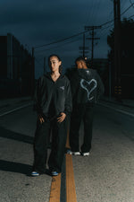 Two people standing on a dark street with wearing INTRA ONE toxic love zip up hoodies with a smoke heart design.